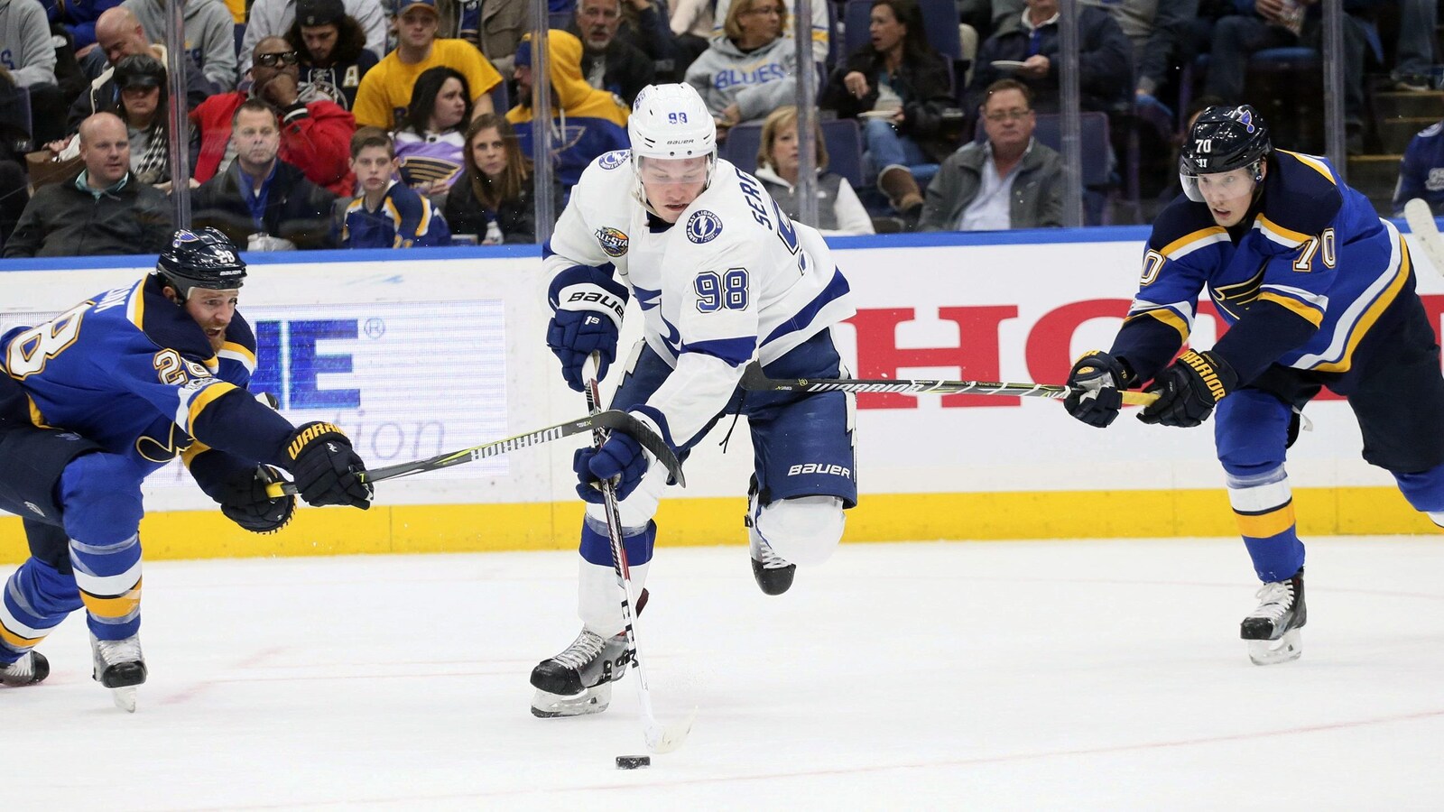 Mikhail Sergachev contrôle la rondelle en évitant deux joueurs des Blues de St-Louis.