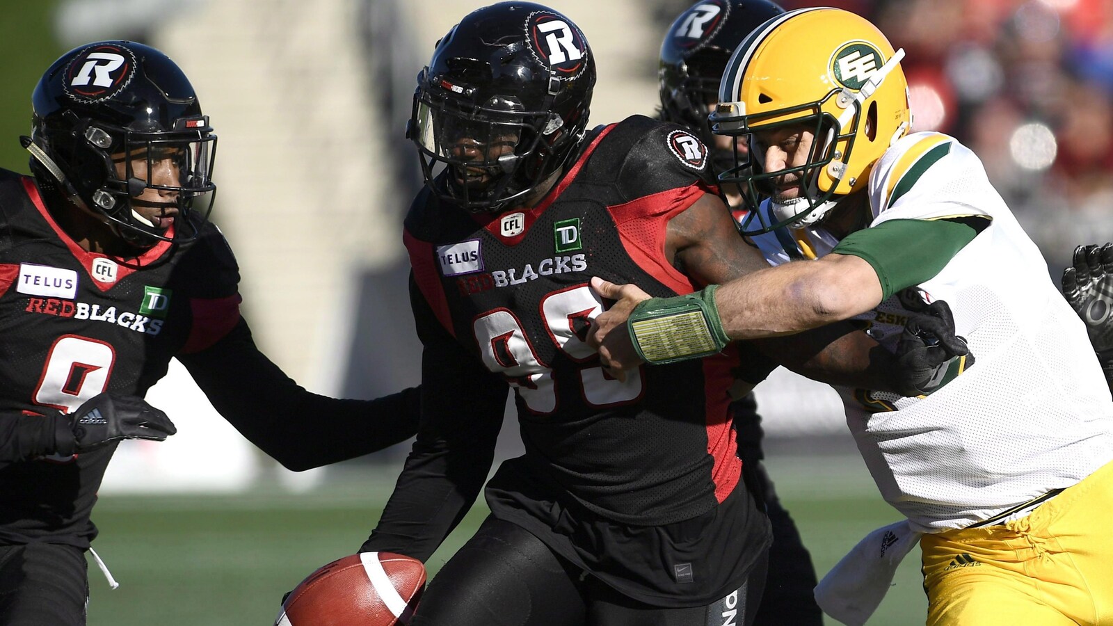 Le joueur de ligne défensive du Rouge et Noir, A.C. Leonard (99) tente de se défaire du quart-arrière des Eskimos Mike Reilly (13).