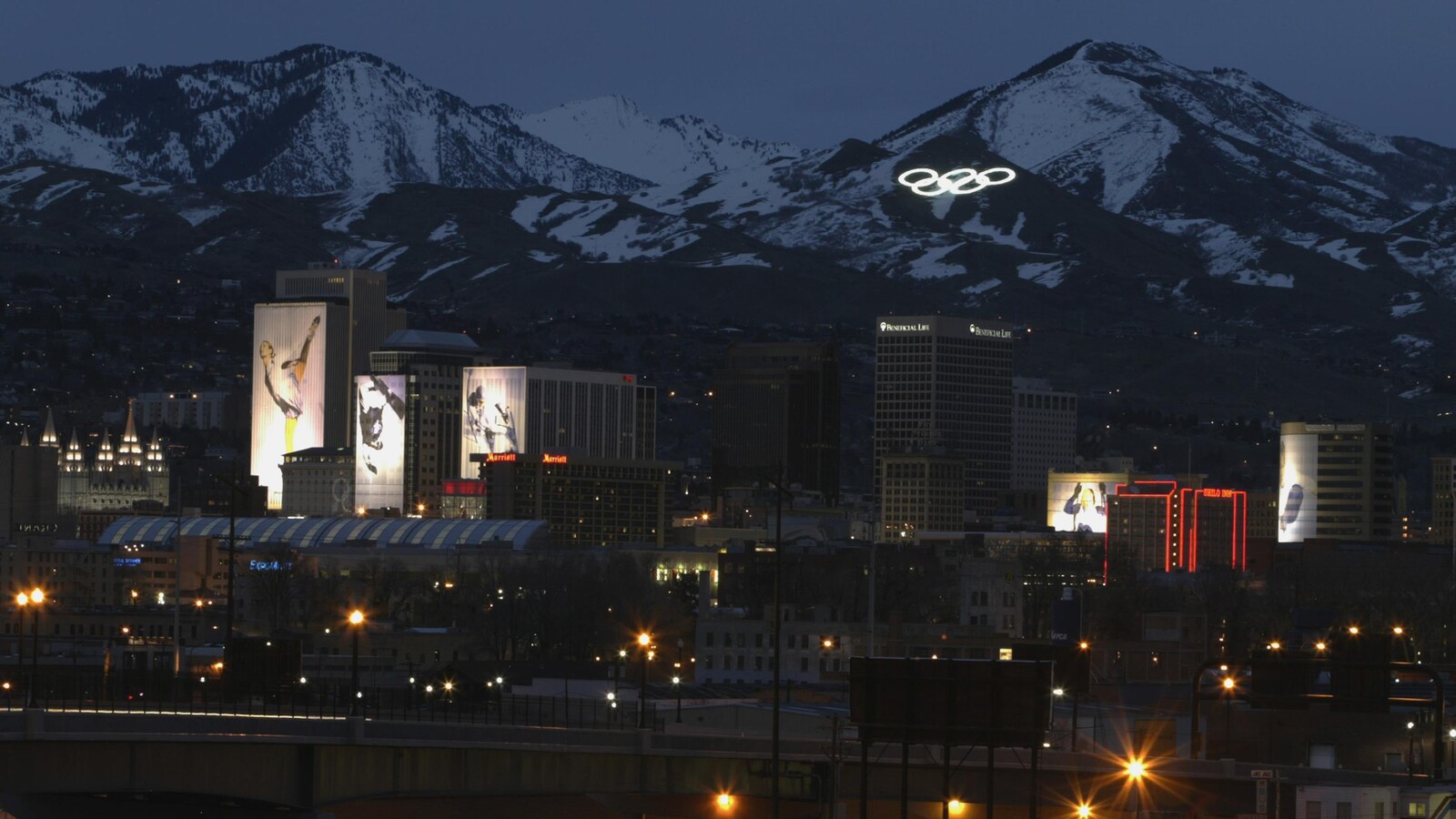 Une vue nocturne du centre-ville de Salt Lake City en février 2002, avec les anneaux olympiques illuminés sur une montagne.