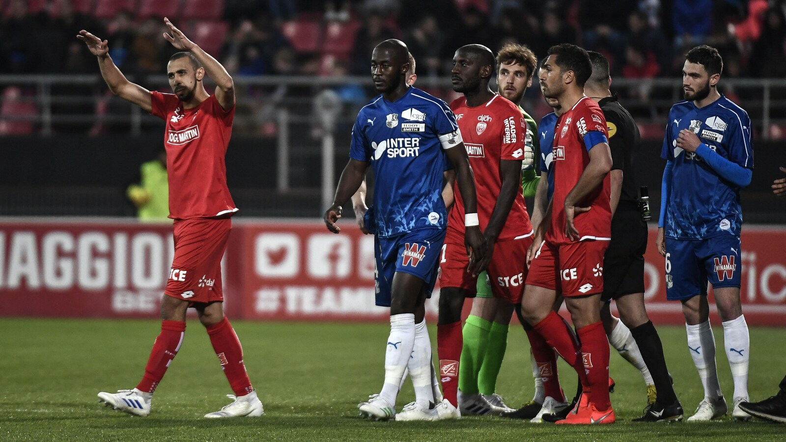 Des joueurs de Dijon et d'Amiens demandent à la foule de se calmer, après que Prince Desir Gouano (au centre), ait expliqué à l'arbitre qu'il a entendu des cris de singe venant de la tribune.