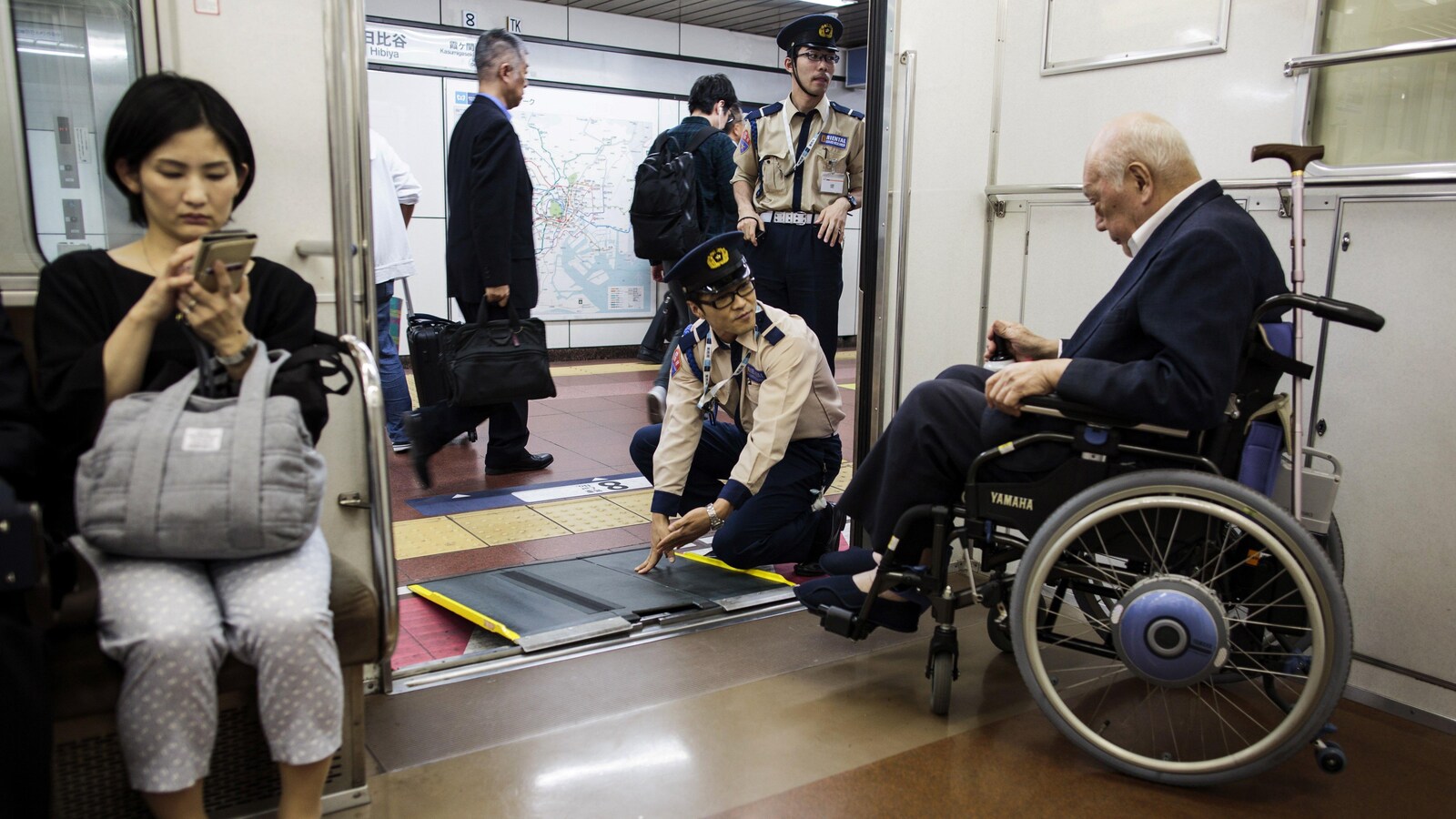Une personne âgée japonaise est aidée à sortir du métro de Tokyo par deux employés.