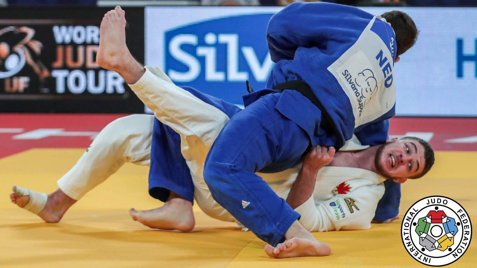 La judoka canadien Zachary Burt, en blanc, est immobilisé au sol par Néerlandais Jesper Smink, en bleu.