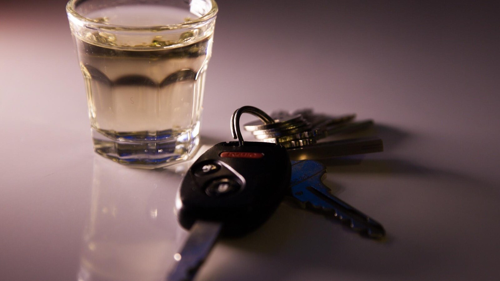 Des clés de voiture et un verre d’alcool posés sur une table blanche.