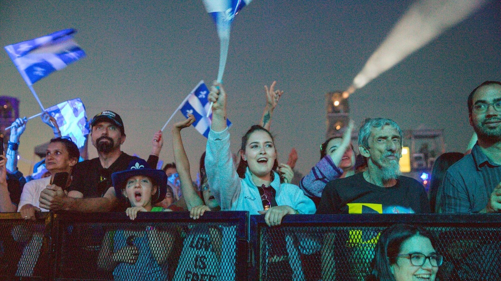 Des gens assistent à un spectacle et agitent des drapeaux du Québec.