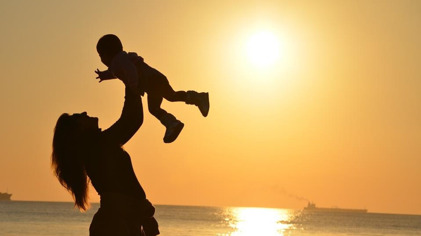 Une mère qui lève son bébé dans les airs devant un coucher de soleil.