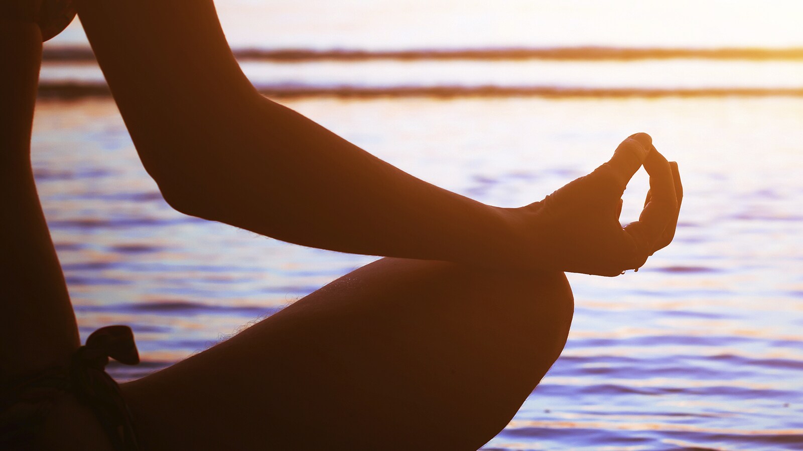 Femme entrain de méditer sur une plage avec les mains en méditation