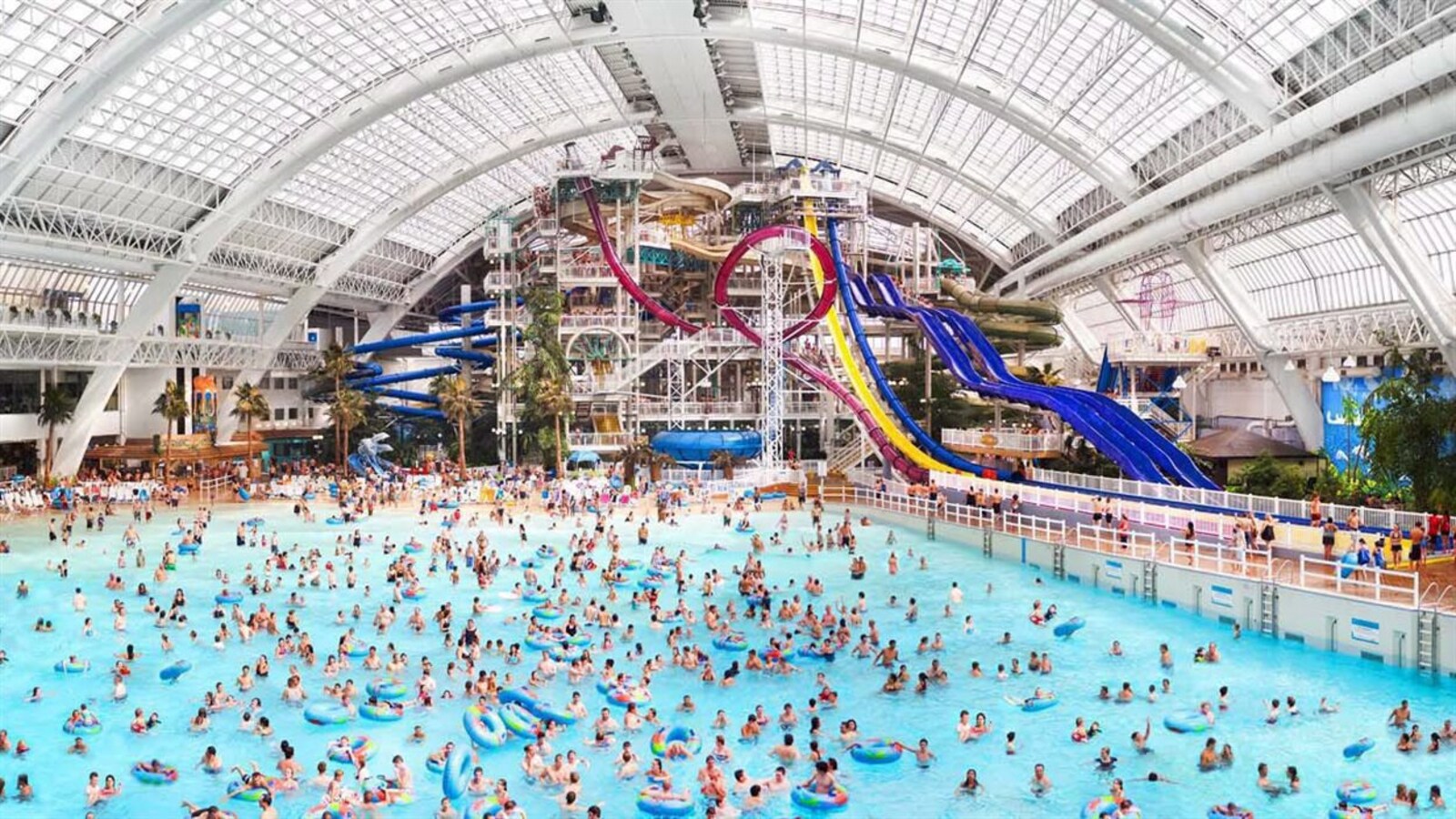 Parc aquatique du West Edmonton Mall : une grande piscine couverte avec beaucoup de monde et des toboggans dans le fond.