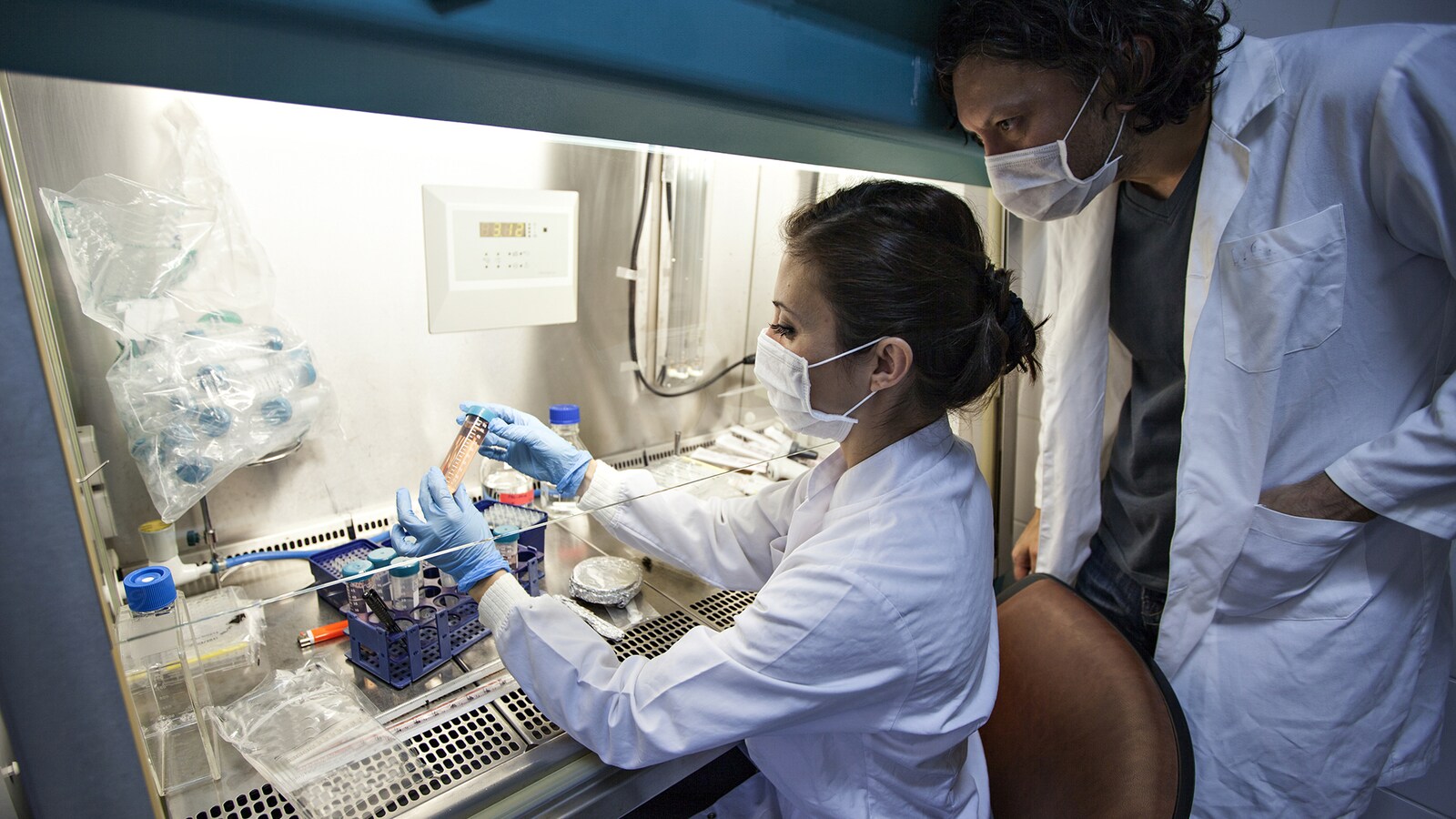 Une chercheuse travaille dans un laboratoire. Un collègue la regarde par-dessus son épaule.