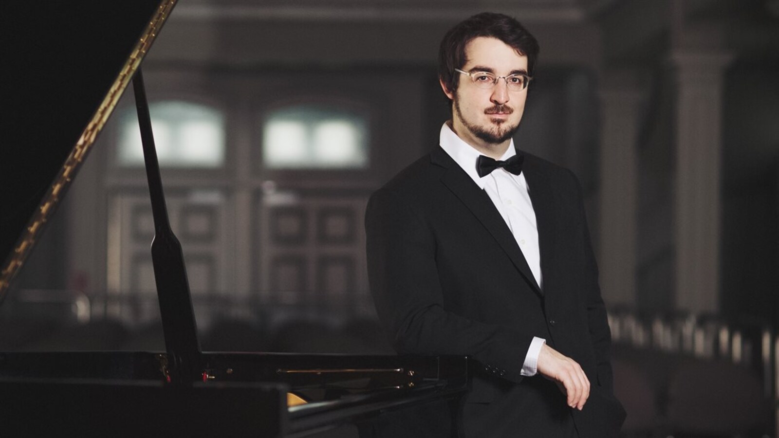 Le pianiste Charles Richard-Hamelin avec un noeud papillon, debout à côté d'un piano.