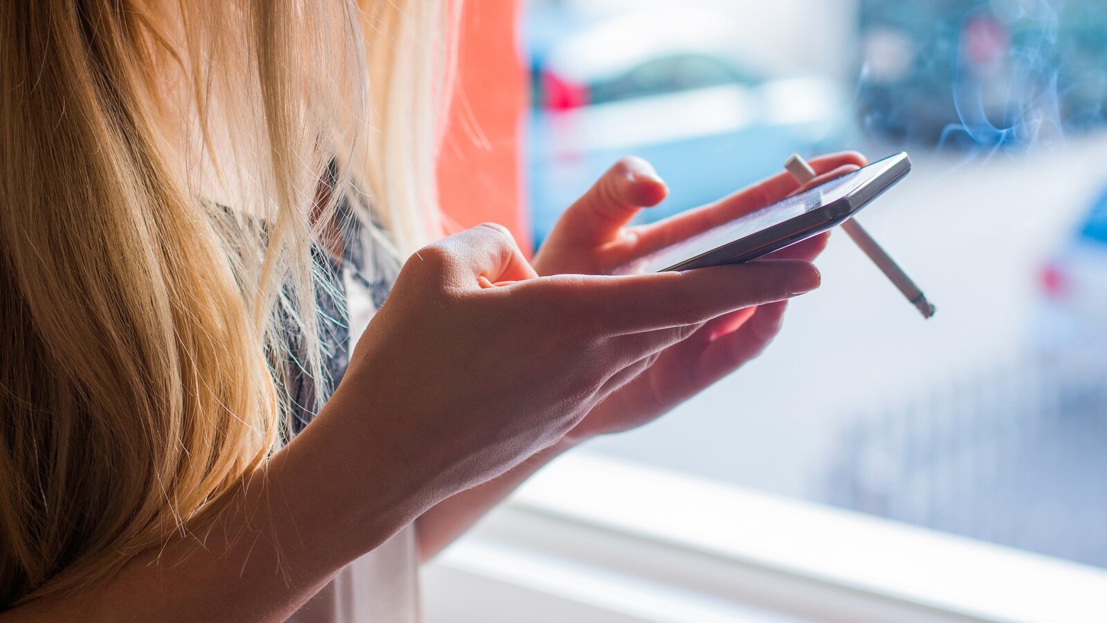 Une jeune femme tape sur un téléphone intelligent en fumant une cigarette.