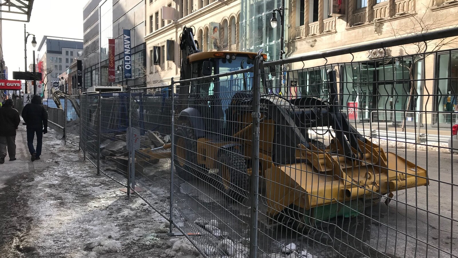 Une clôture empêche la circulation sur la rue Sainte-Catherine, au centre-ville de Montréal, et de la machinerie lourde est stationnée devant les magasins.