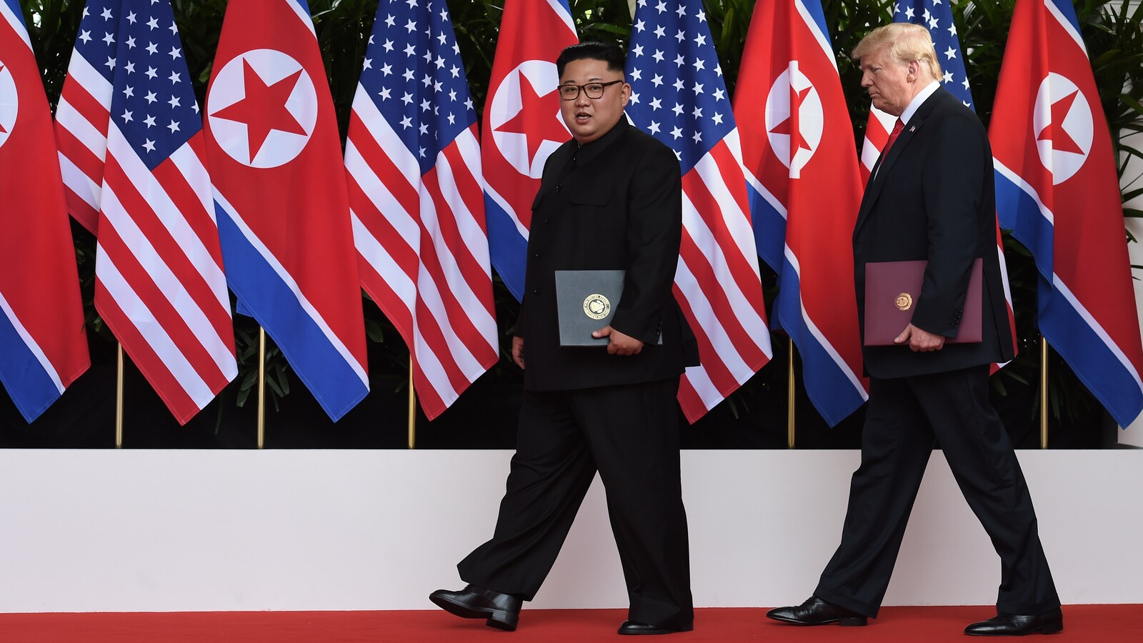 Kim Jong-un et Donald Trump marchent devant des drapeaux de leur pays respectif.