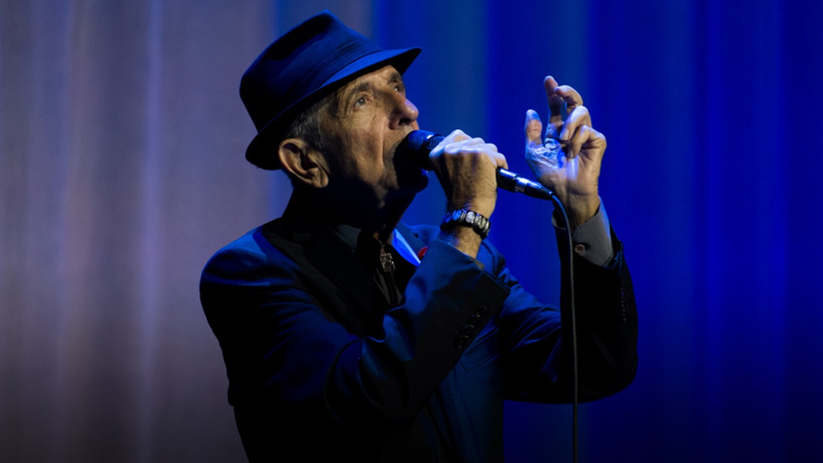 Leonard Cohen chante sur une scène au fond bleu.