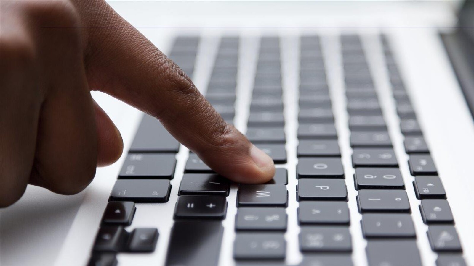 Gros plan sur une main dont un doigt appuie sur une touche de clavier d'ordinateur.