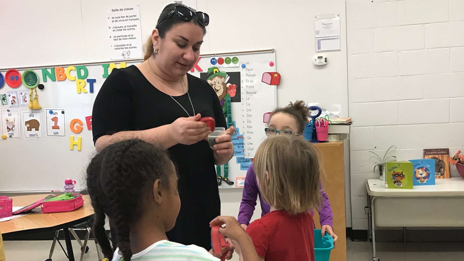 L'enseignante Gayané Deval est en classe avec trois élèves de maternelle devant un tableau.