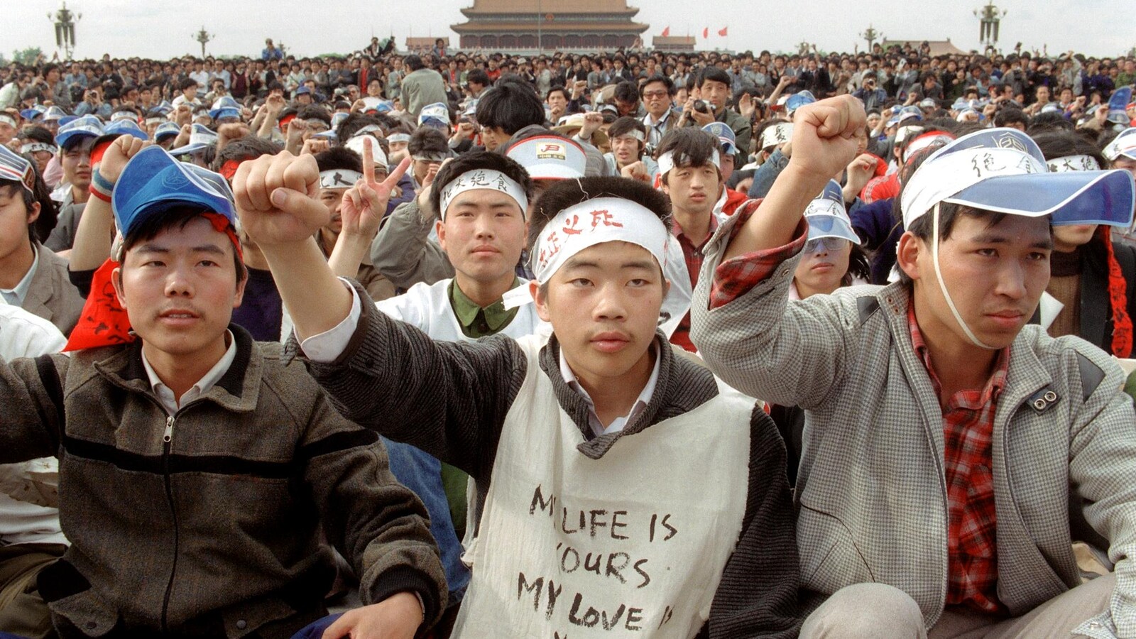 Des jeunes chinois sont assis sur la place Tiananmen en levant le poing en signe de protestation.