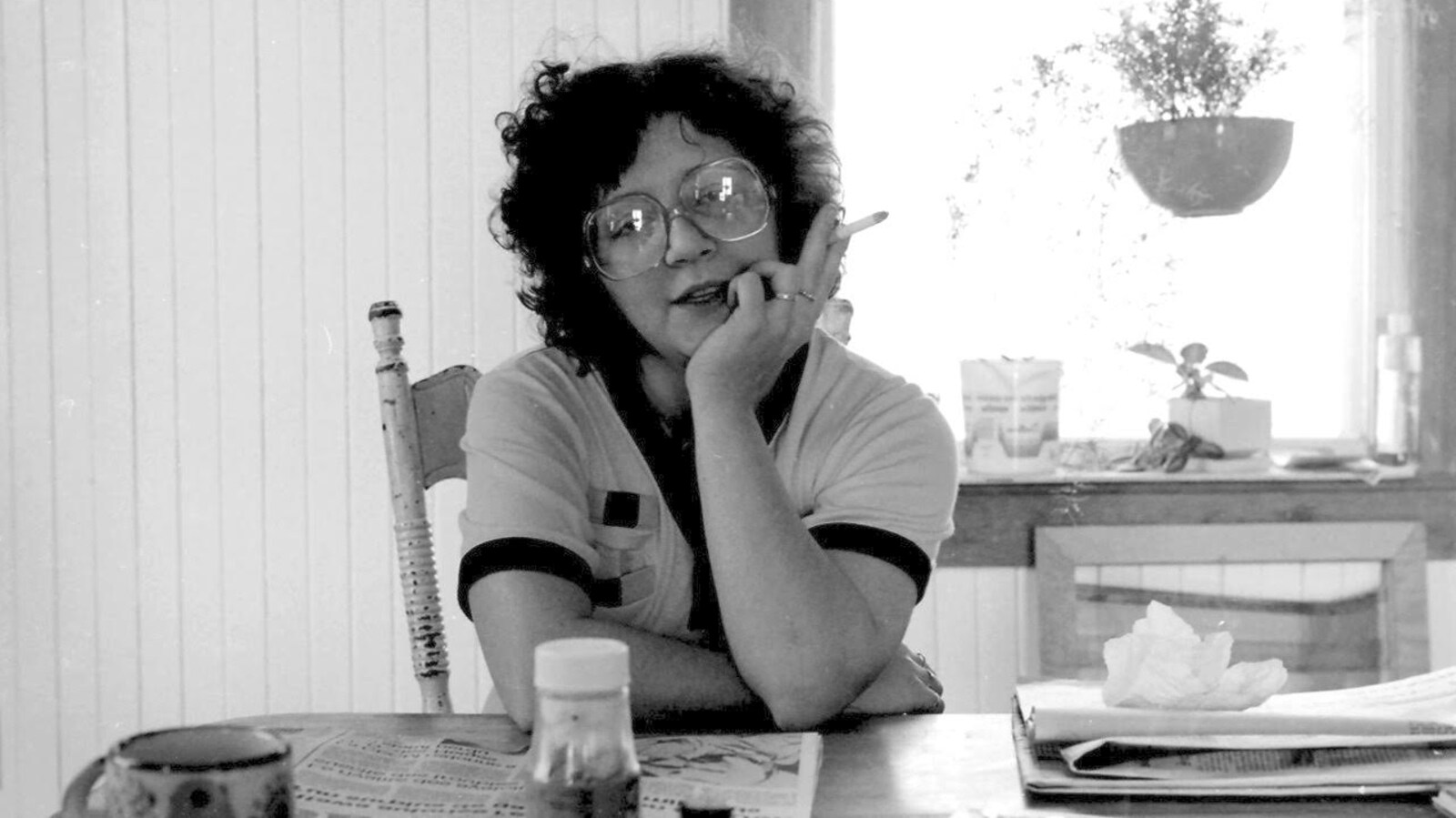 Une femme assise dans une cuisine tient une cigarette dans sa main.