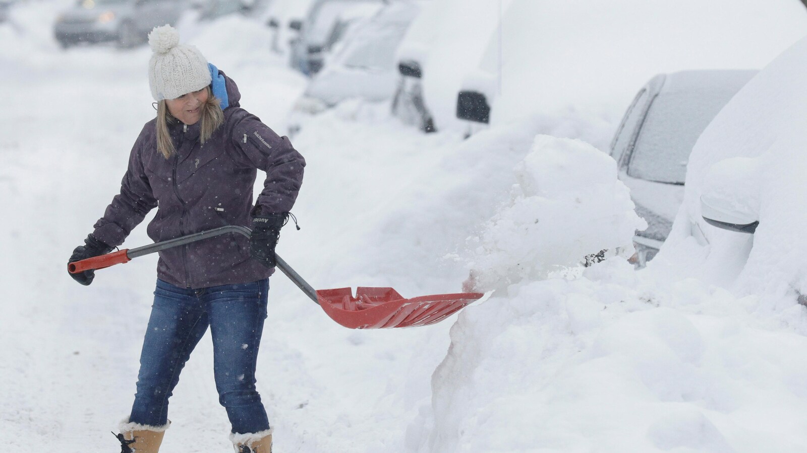 Une femme pellette la neige pour libérer sa voiture dans les rues de Montréal.