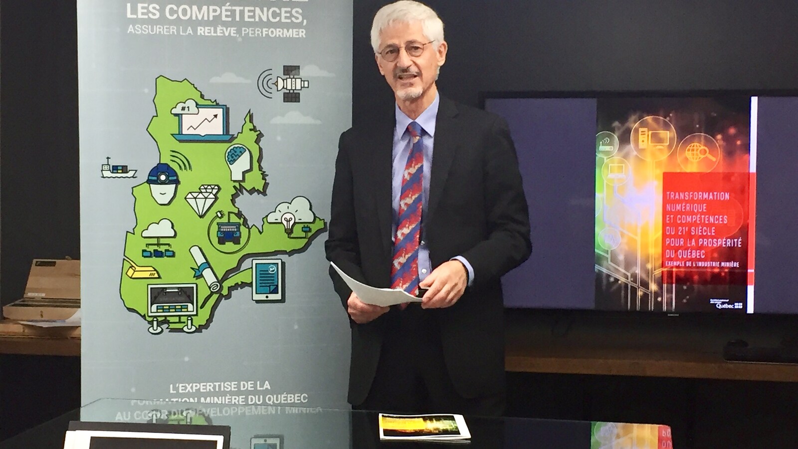 Robert Marquis, PDG, Institut national des mines du Québec est devant un écran pour la présentation du rapport Transformation numérique et compétence du 21e siècle pour la prospérité du Québec, exemple de l'industrie minière.