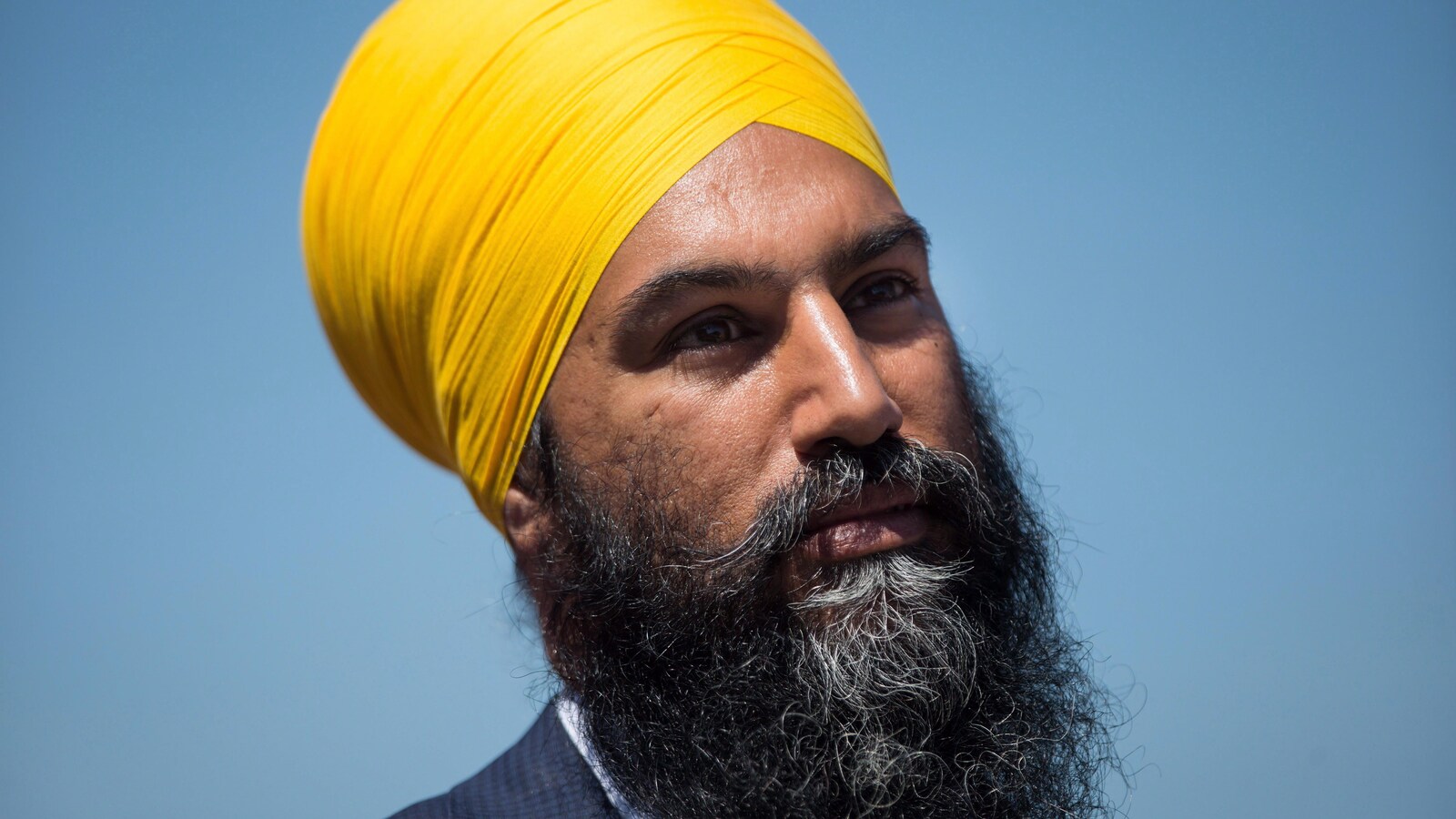 Un homme avec un turban jaune est photographié plan épaule sur fond bleu.