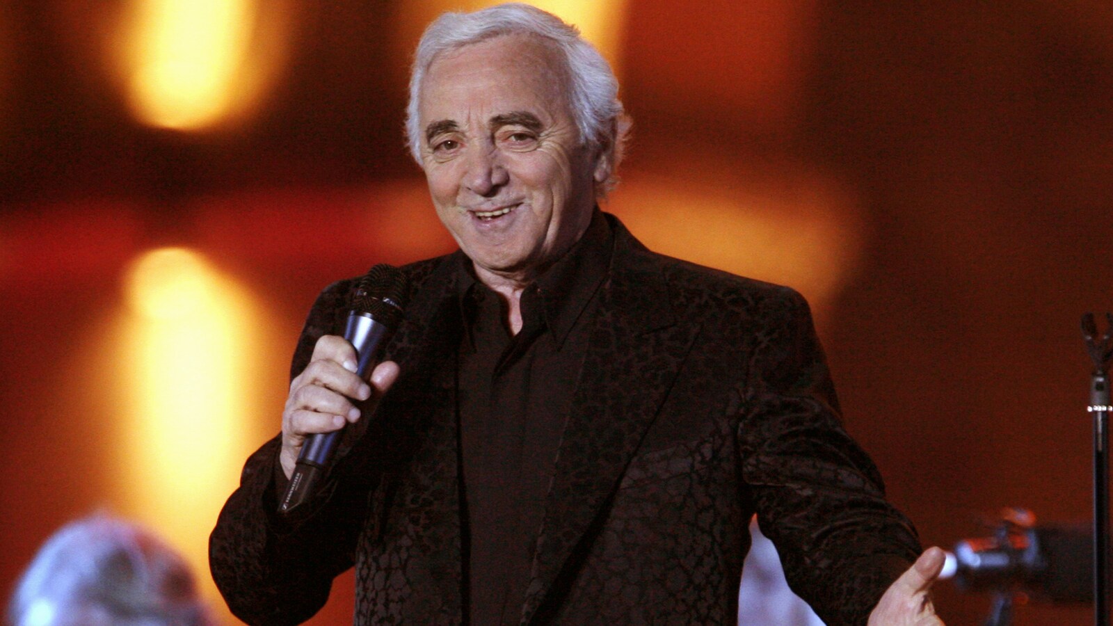 Charles Aznavour chante et sourit.