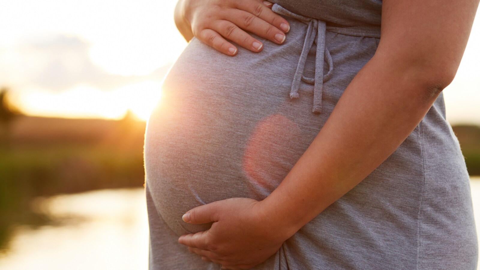 Une femme enceinte devant un coucher de soleil.