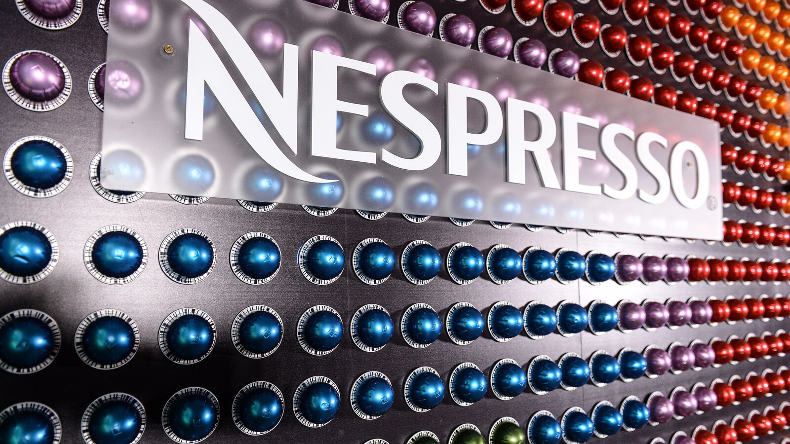Un mur de dosettes jetables multicolores derrière le logo de la compagnie Nespresso