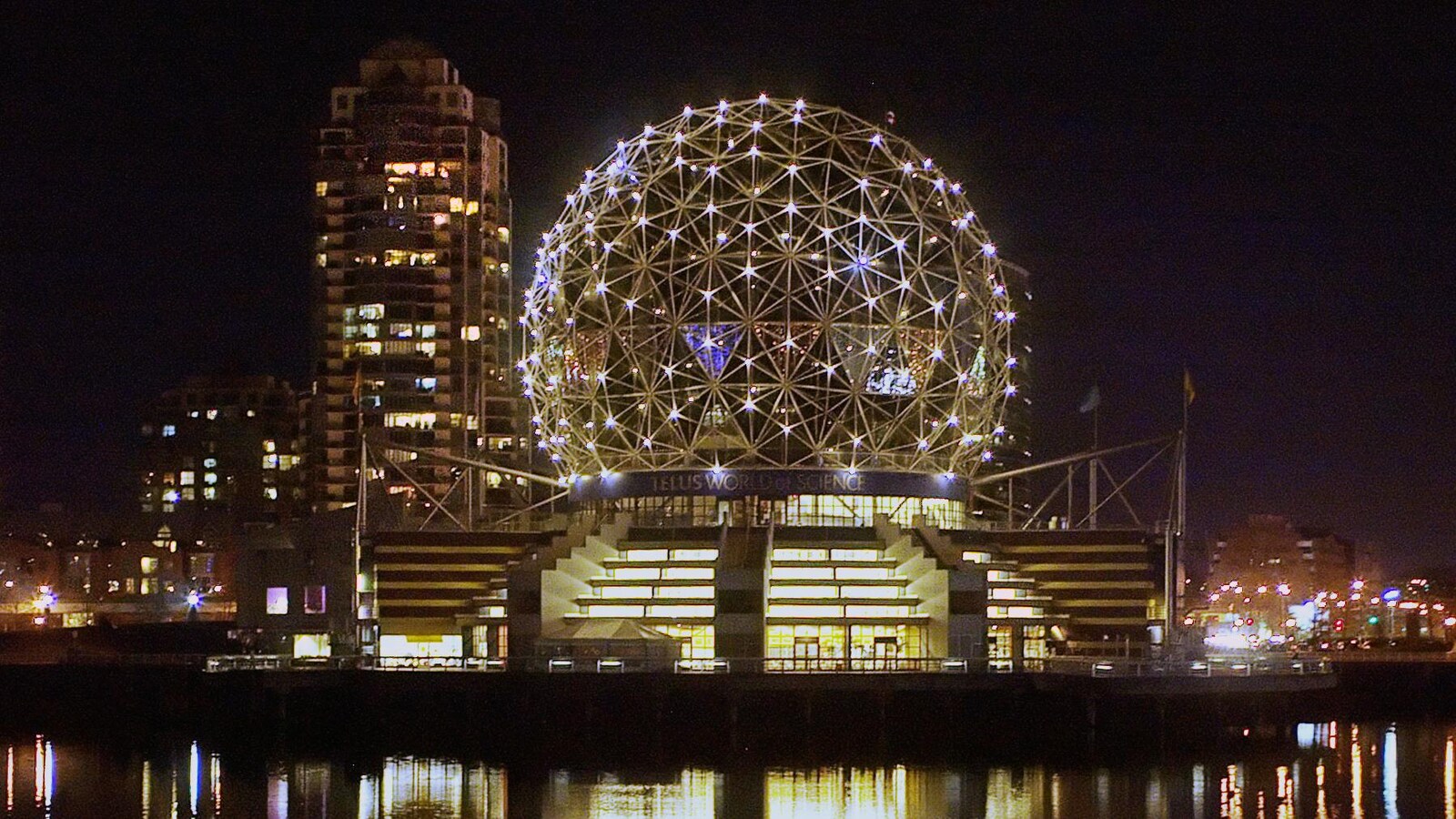 La structure en forme de boule du musée est illuminée et se reflète dans l'eau de la rivière la nuit.