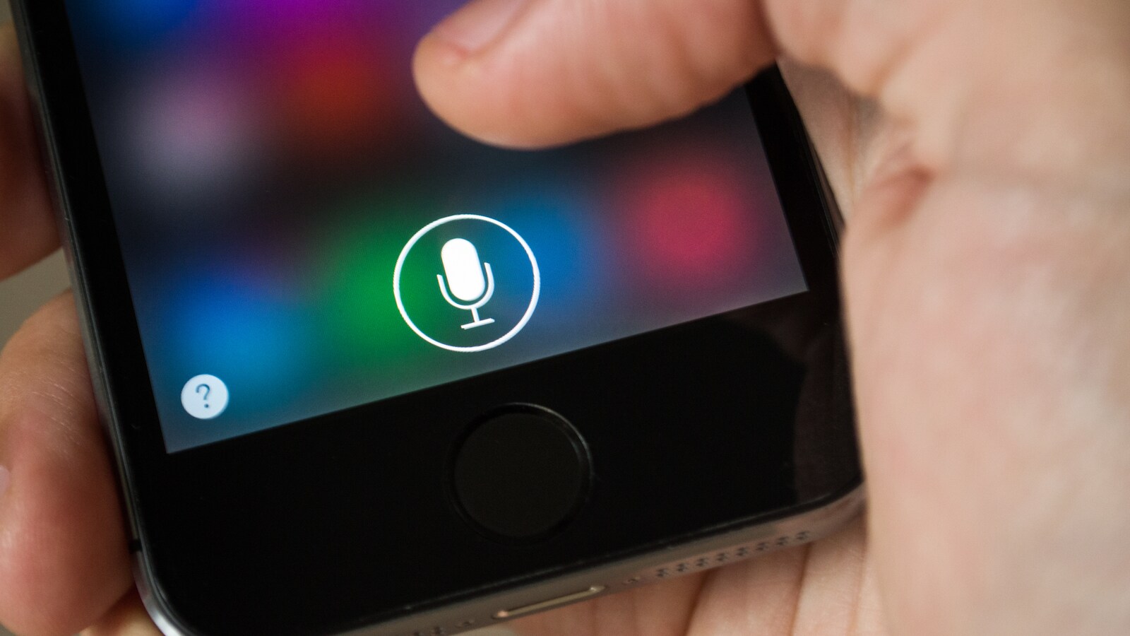 Un gros plan sur l'écran d'un iPhone dans la main d'une personne. Une icône de micro est affichée à l'écran du téléphone.