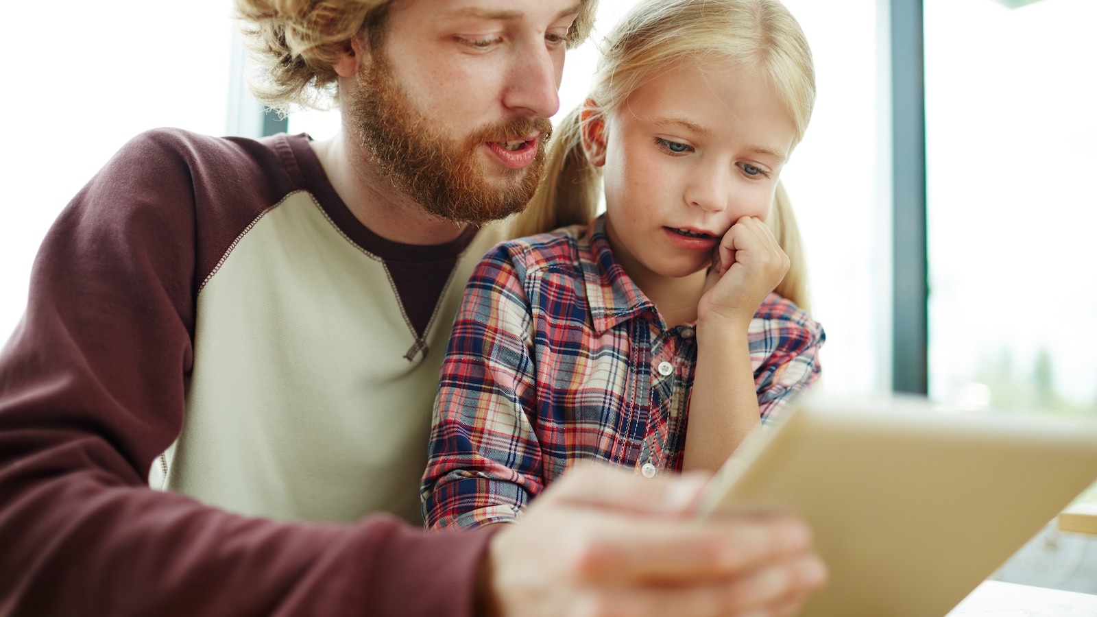 Un père tient une tablette électronique et la montre à sa fille.