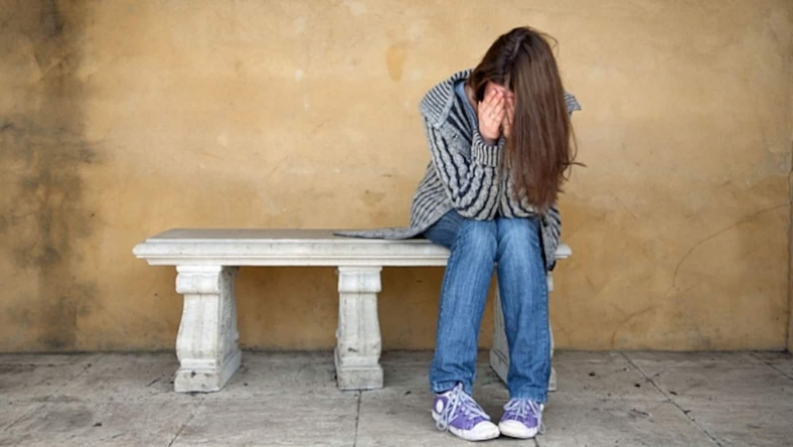 Une jeune fille se tient le visage entre les mains, elle est assise sur un banc.