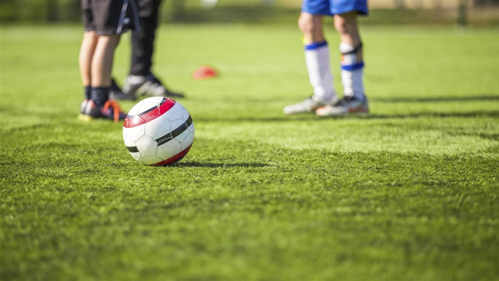 Un ballon de soccer sur un terrain de gazon devant de jeunes joueurs.