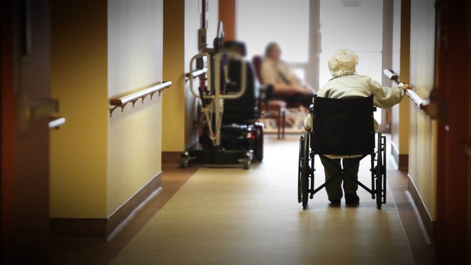 Une dame dans un fauteuil roulant dans le couloir d'un CHSLD.