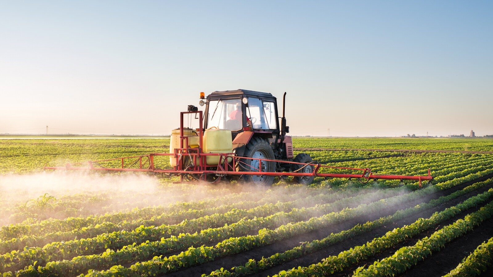Un tracteur épand des pesticides dans un champ de soya.