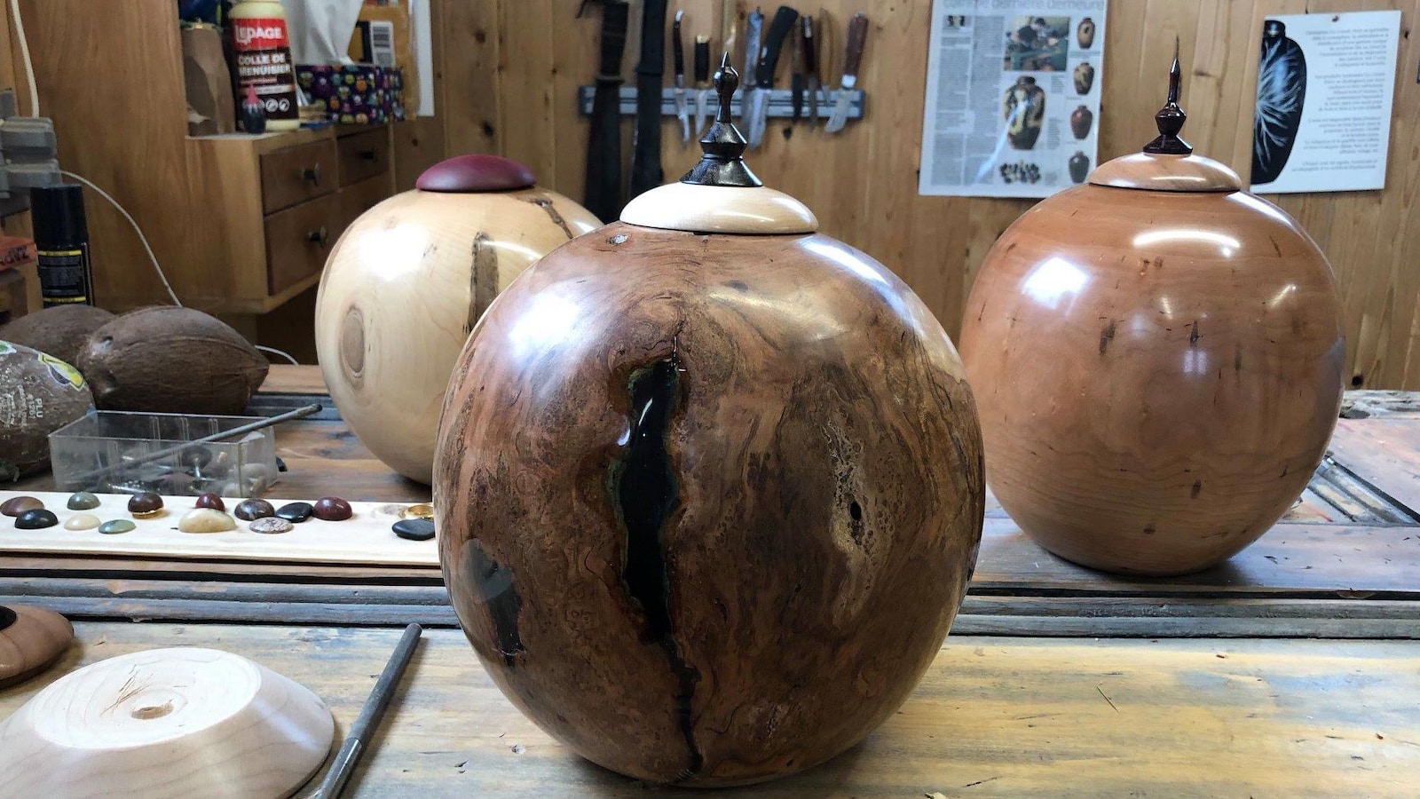 Trois urnes funéraires rondes en bois noueux déposées sur une table d’ébéniste