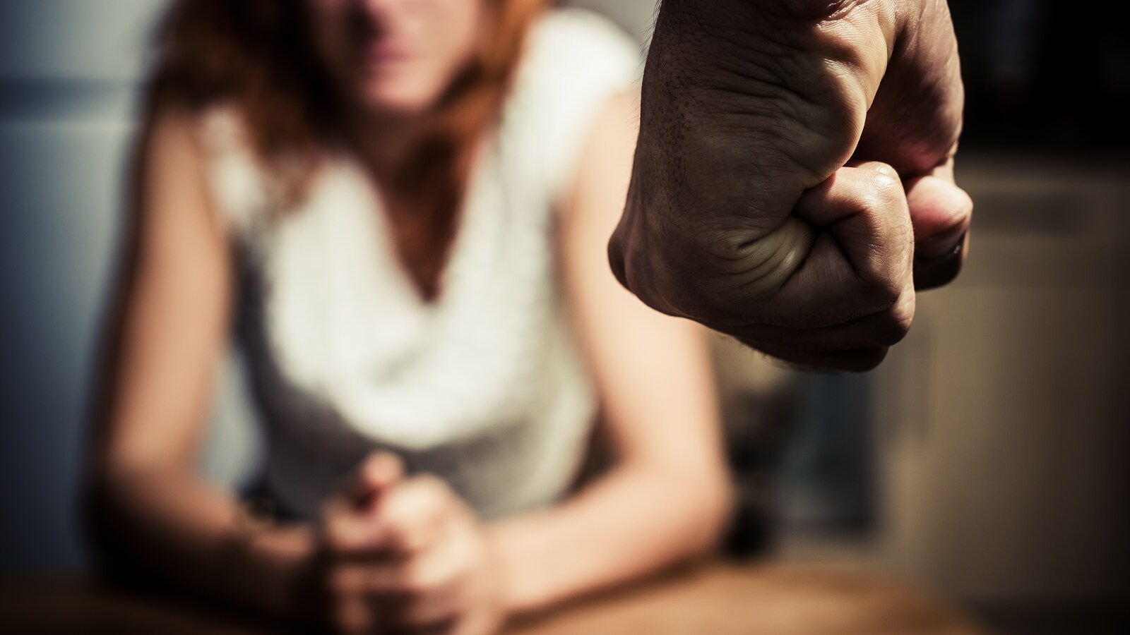 Le poing d'un homme se serre, une femme est en arrière-plan.