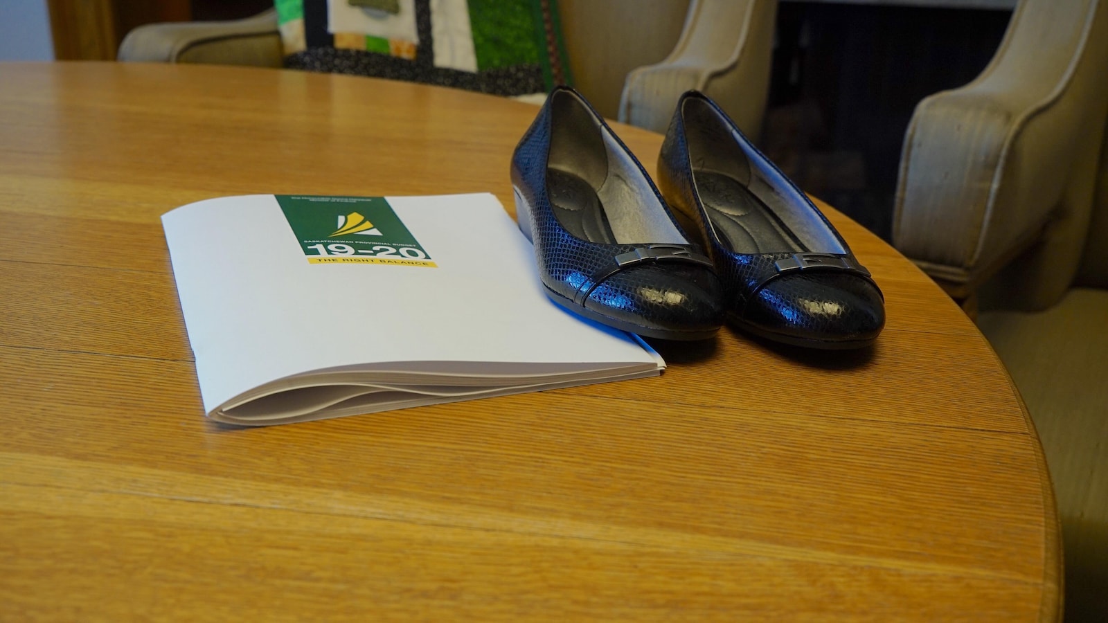 Une paire de chaussures noires déposée sur une table à côté d'une version imprimée du budget 2019-2020.