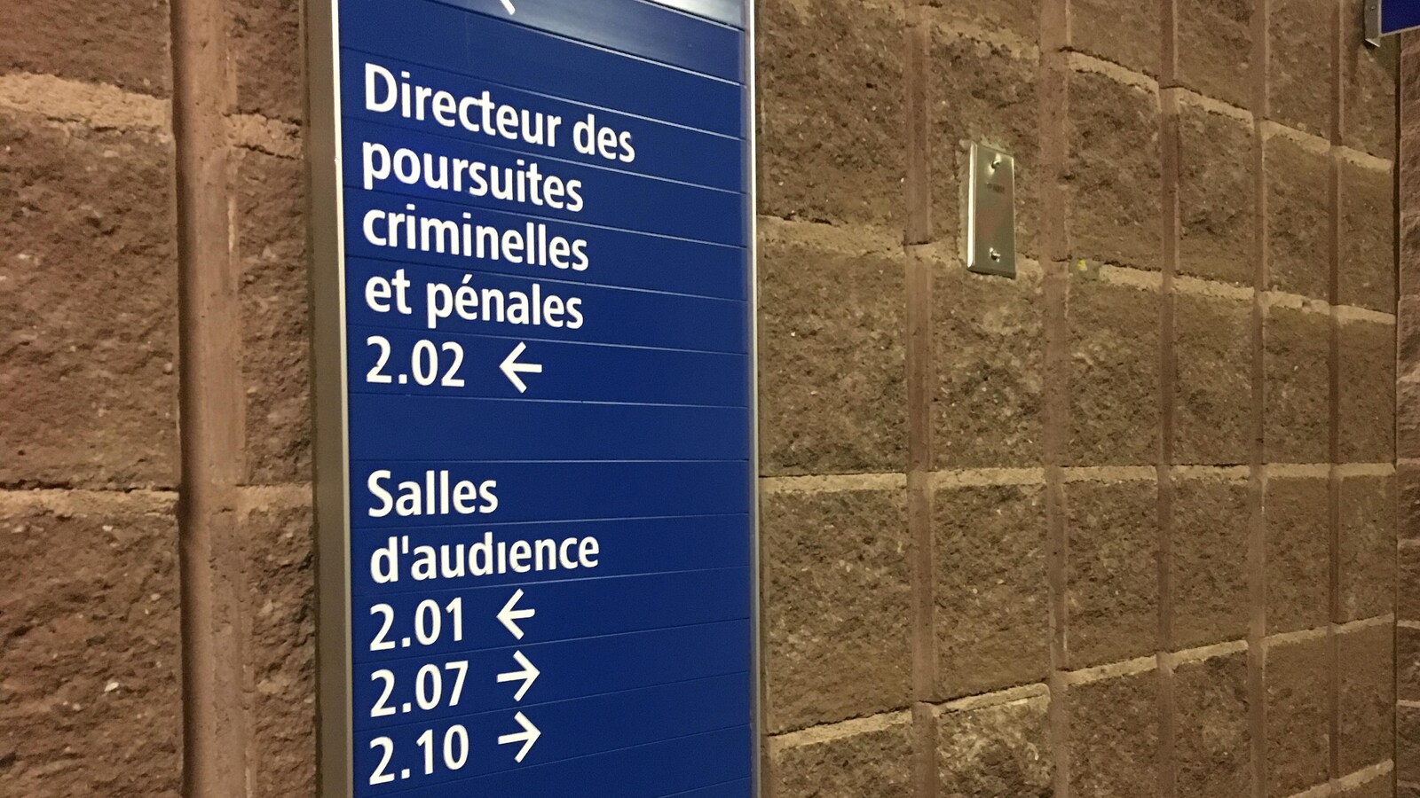 Panneau d'indication sur un mur du palais de justice de Chicoutimi indiquant la direction à prendre pour les bureaux du directeur des poursuites criminelles et pénales