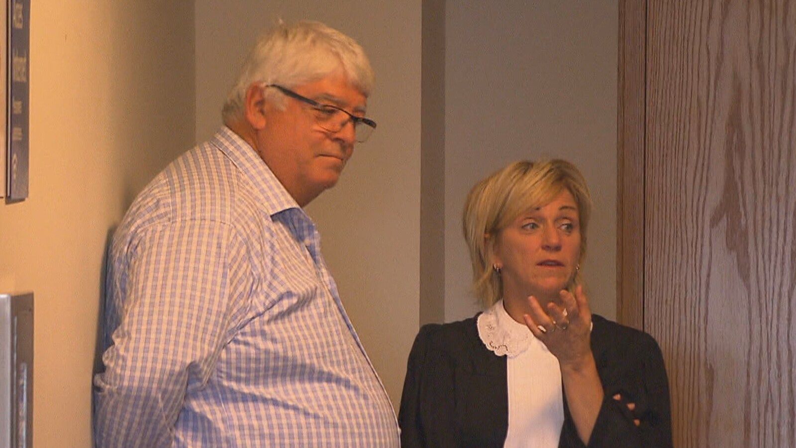 Mario Gauthier est adossé au mur d'un corridor du palais de justice de Chicoutimi en compagnie de son avocate.