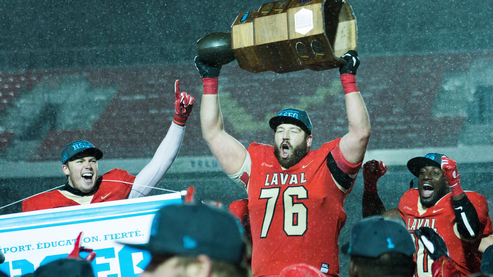 Samuel Thomassin tient la Coupe Vanier à bout de bras sous la neige entouré de deux coéquipiers
