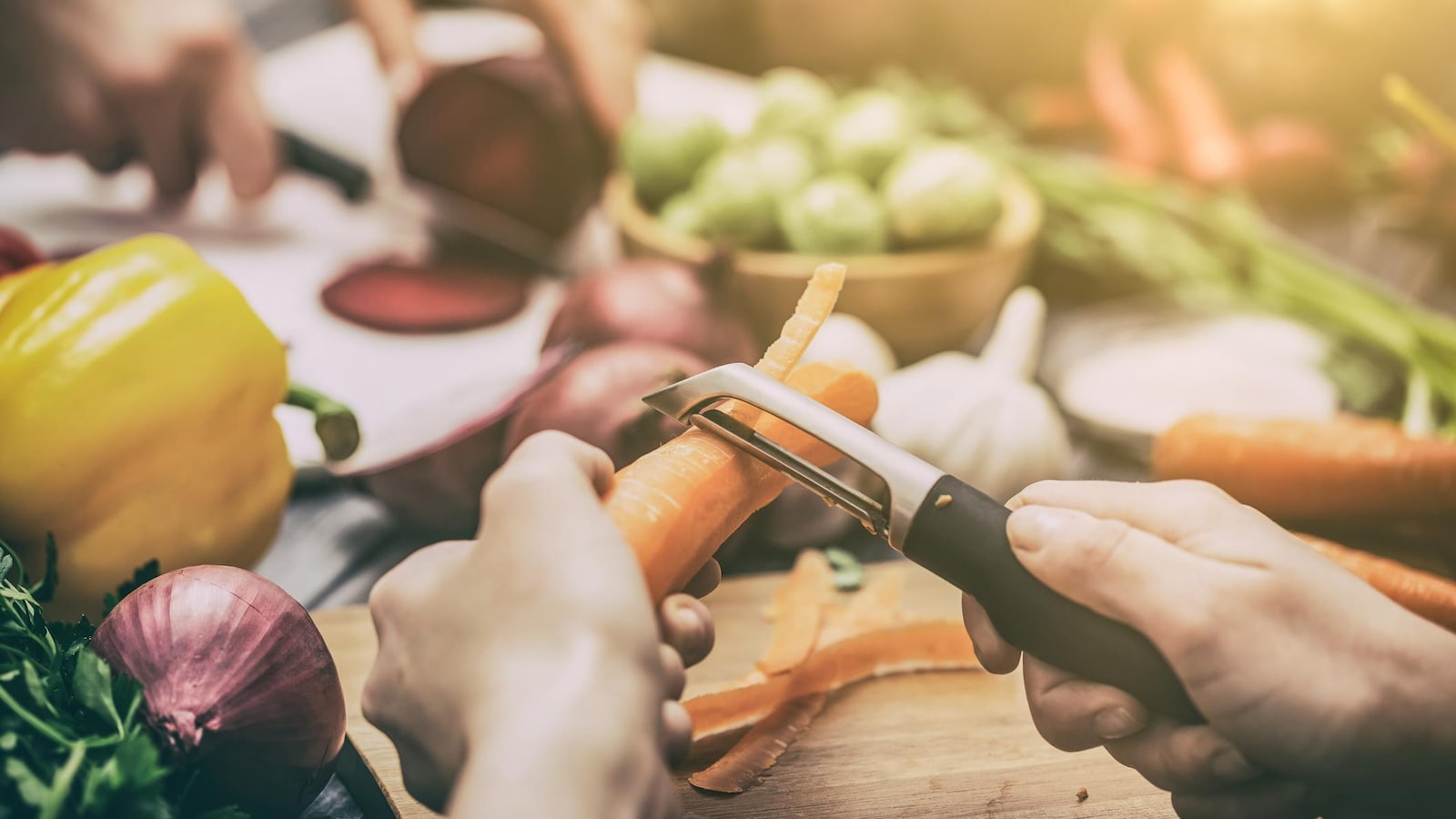 Une personne qui épluche une carotte sur un plateau de légumes.