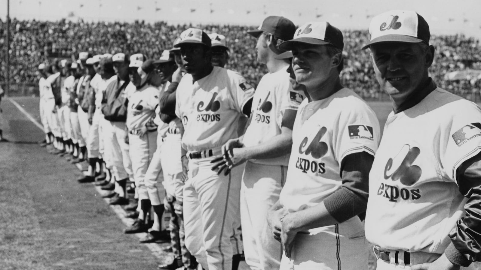 Joueurs et entraîneurs des Expos de Montréal, dont le gérant Gene Mauch (à l'extrême gauche), alignés lors de la présentation du premier match de l'équipe, à domicile, au parc Jarry, à Montréal.