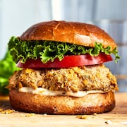 Un burger au poulet croustillant garni de tomates, de salade et d'une sauce.