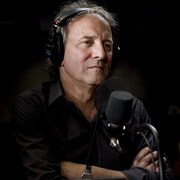 Assis en studio, l'artiste écoute la question de l'animatrice.