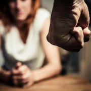 Un poing fermé en avant-plan, et une femme les yeux baissés en arrière-plan.