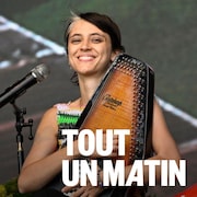 La chanteuse Pomme souriant lors d'un concert avec une autoharp dans les mains.