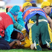 Étendu par terre, un joueur de rugby est entouré de cinq soigneurs.