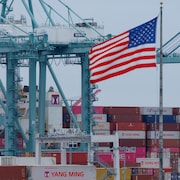Un drapeau américain devant des conteneurs dans un port.