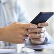 Un jeune homme adulte envoyant des messages texte tout en tenant un smartphone pendant la journée.