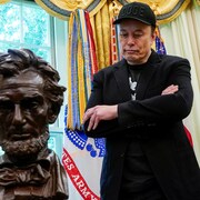Elon Musk, v&ecirc;tu de noir les bras crois&eacute;s, regarde vers le bas. Un buste en bronze d'Abraham Lincoln est devant lui.